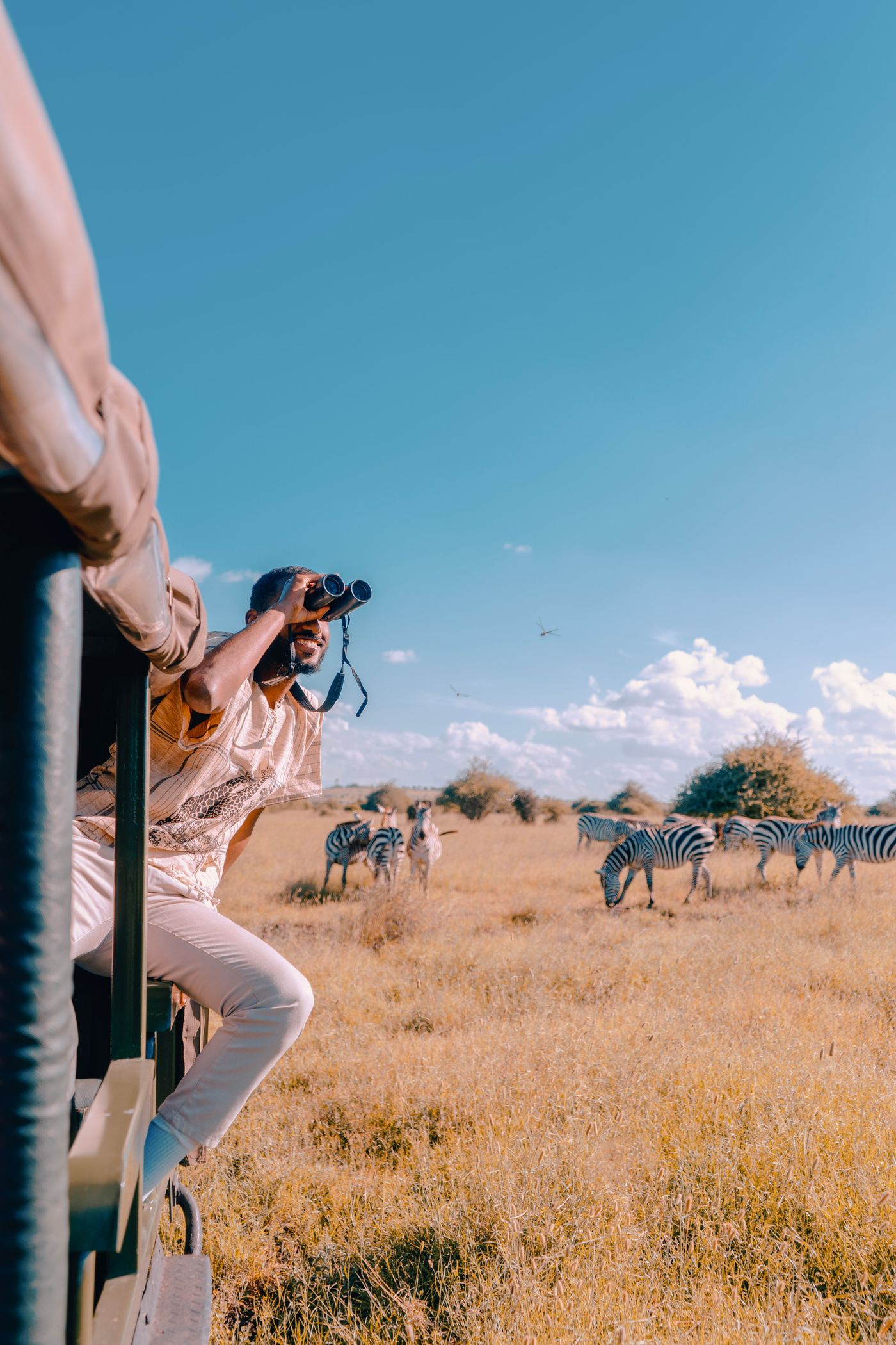 Traveler observing a herd of zebras from a safari vehicle on the Kenyan savanna